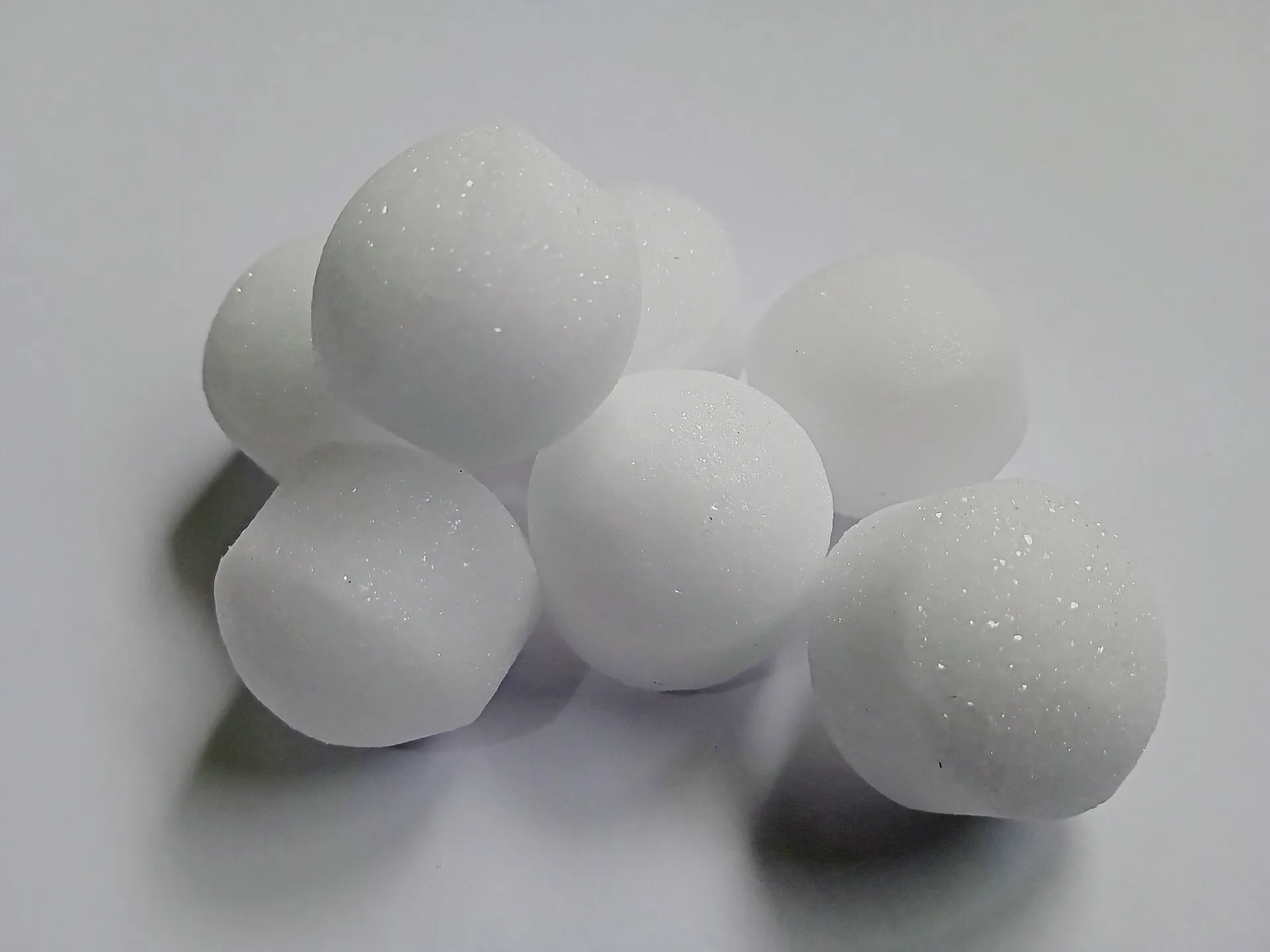 Sept boules antimites blanches, rondes et légèrement granuleuses, posées sur un fond blanc